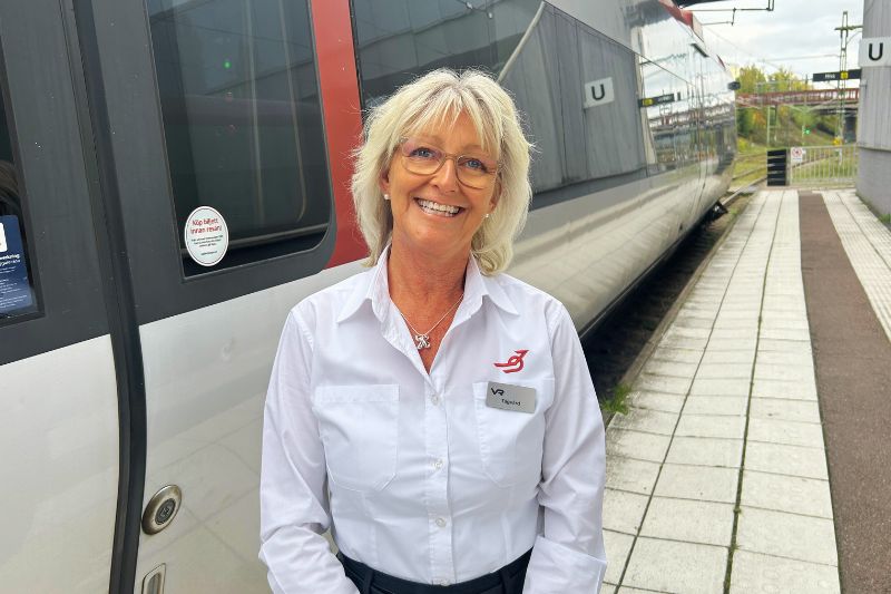 Kvinna som står framför ett tåg, på perrongen. Hon arbetar som tågvärd och heter Pia
