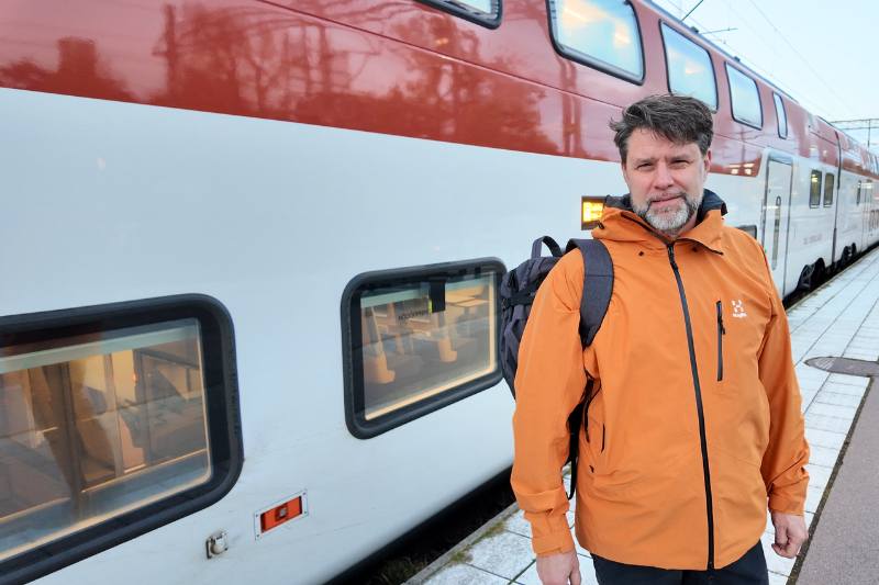 Man med orange jacka står framför tåget, dubbeldäckare.