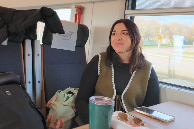 Kvinna sitter i tåget Er1, dubbeldäckare. sitter i tåget med termos framför , vid bordet. mörk hårig kvinna.