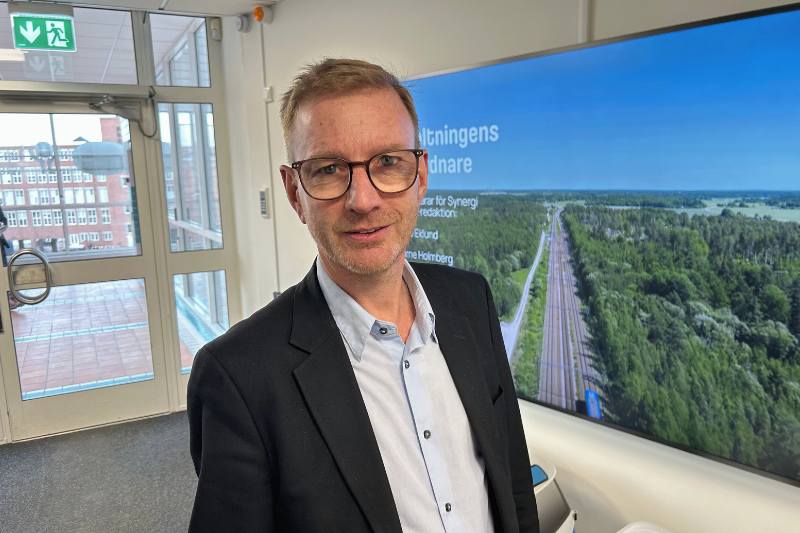 Krister, chef för kundservice. Med kavaj och blå skjorta står framför en tv. Glasögon och medelljus hår.