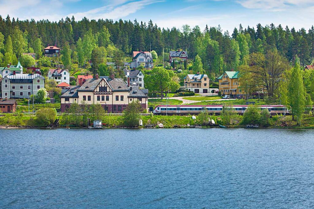 Reginatåg som åker in i ängelsberg, stationshus intill vatten. En sommardag.